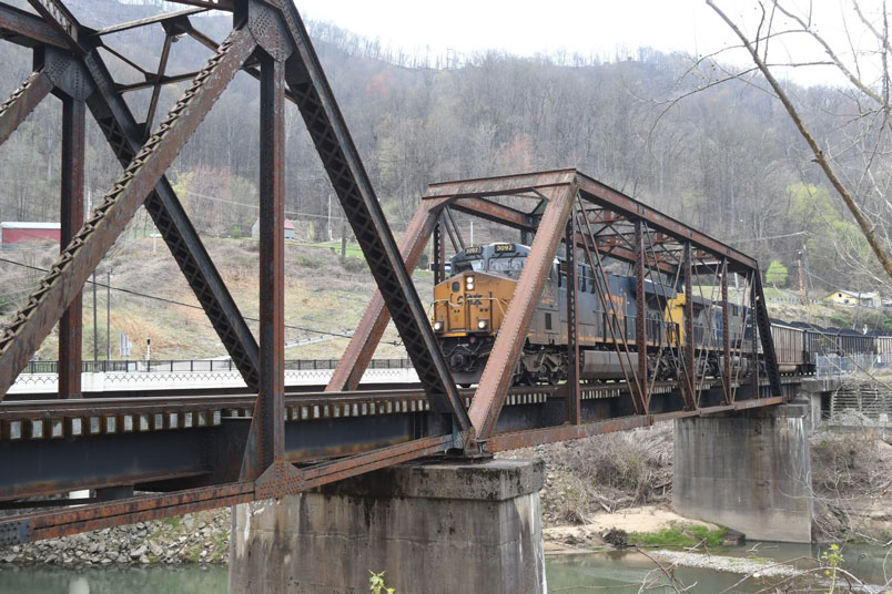 R209-29 with the same engines as the afternoon before brings the remaining 55 loads toward the yard to make a 110-car train. This bridge is composed of three distinct structures. The nearest is a riveted through truss built in 1920. The second is a pin-connected through truss built in 1904. The third is a deck plate girder bridge also built in 1904. Why the first truss is newer than the other two is unknown.