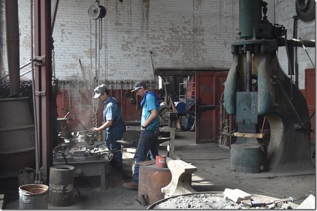 An apprentice blacksmith and his helper working in the blacksmith shop.